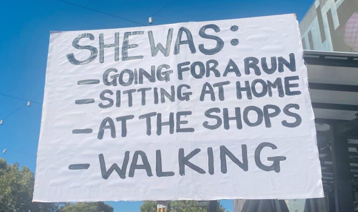 An anti-violence against women protest sign reading “She was...going for a run, sitting, at home, at the shops, walking.”