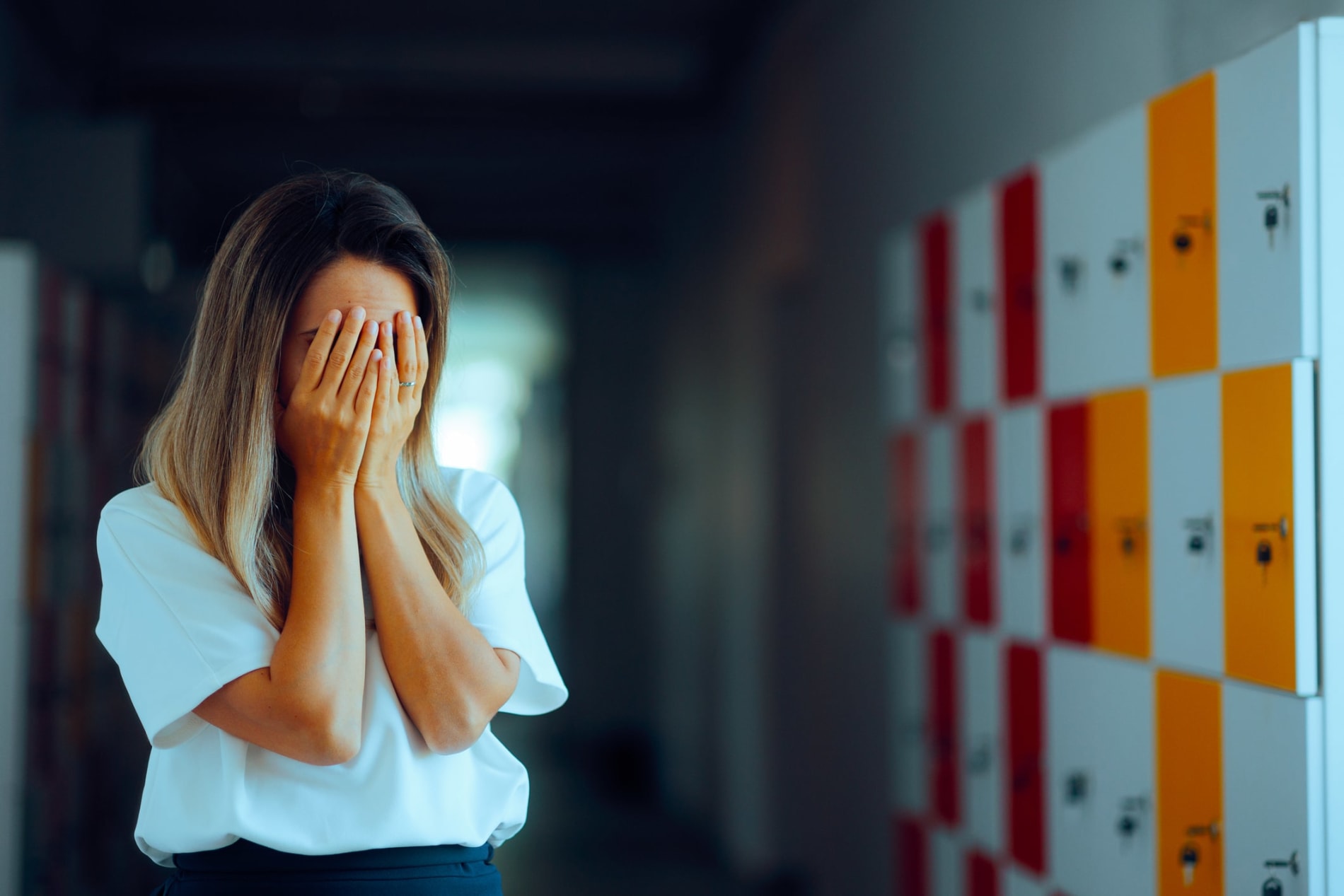 Distraught female teacher with her face in her hands in a school corridor