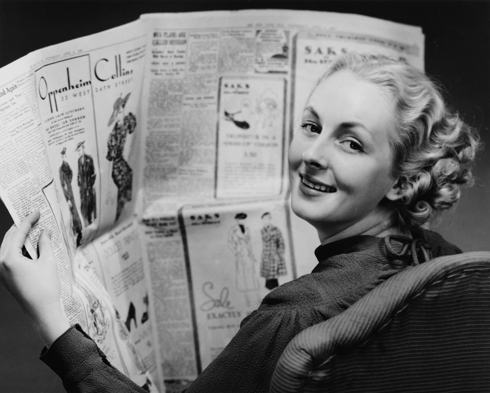 A woman reads a newspaper with a number of large fashion advertisements.