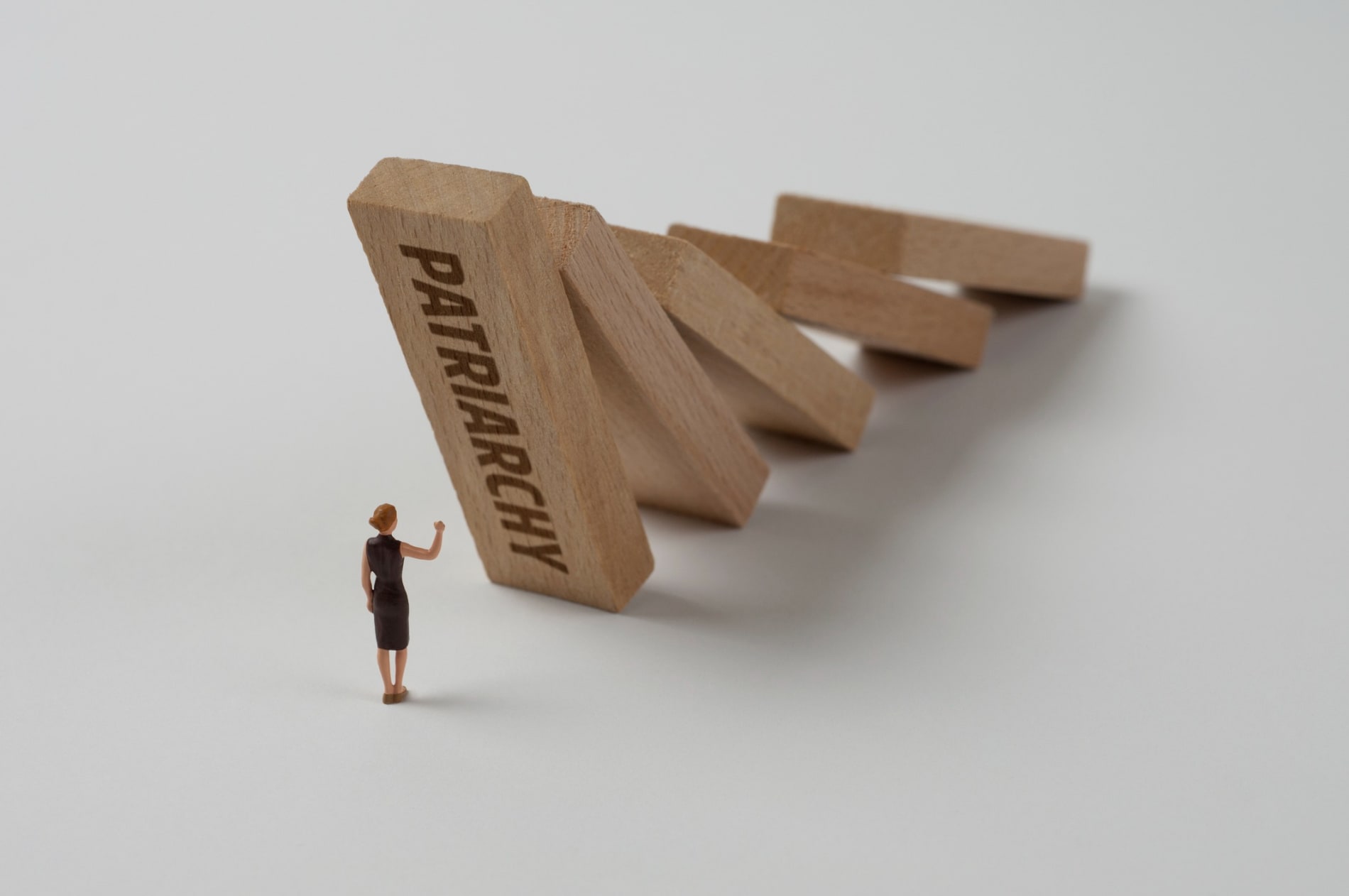 Female toy figure in front of falling wooden blocks with patriarchy written on one of them.