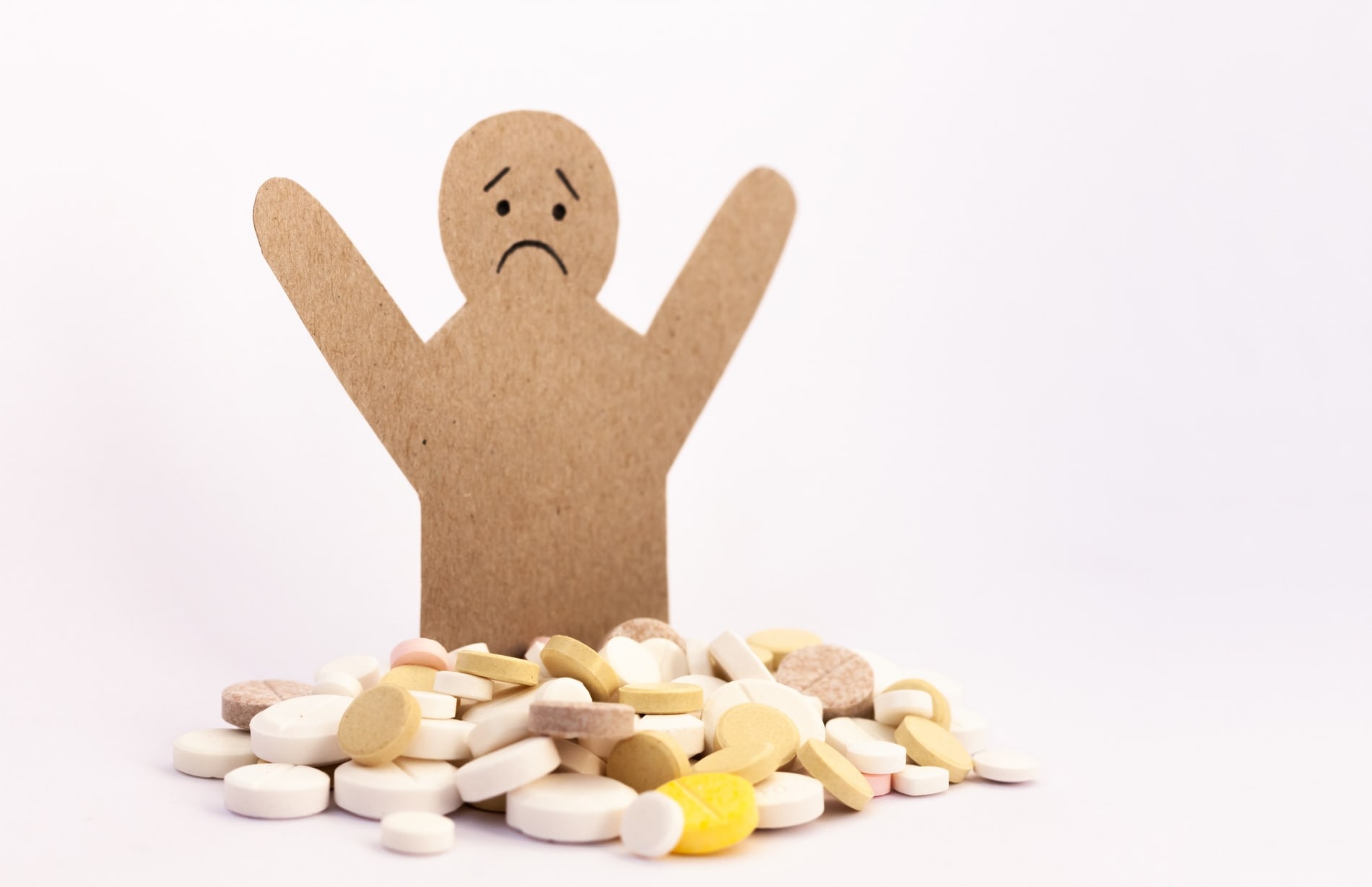 Cardboard figurine looking sad in front of a pile of pills