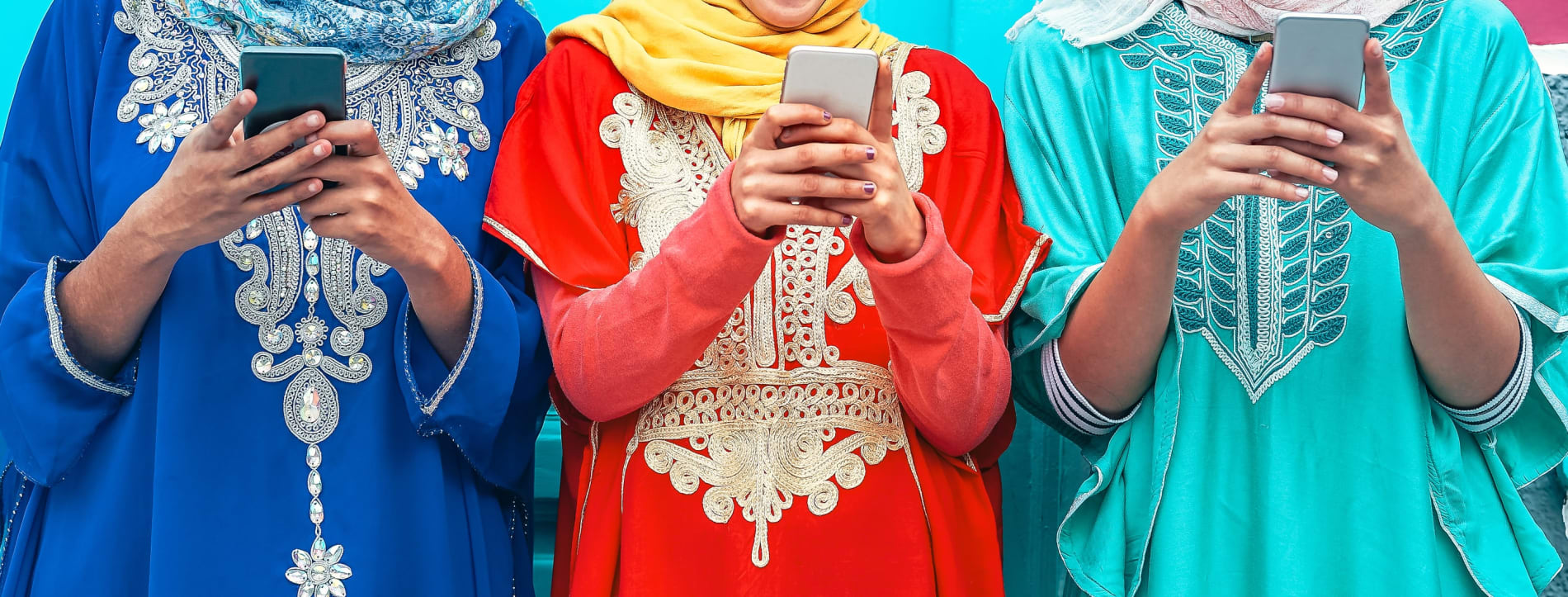 Three Muslim girls standing side by side using their mobile phones