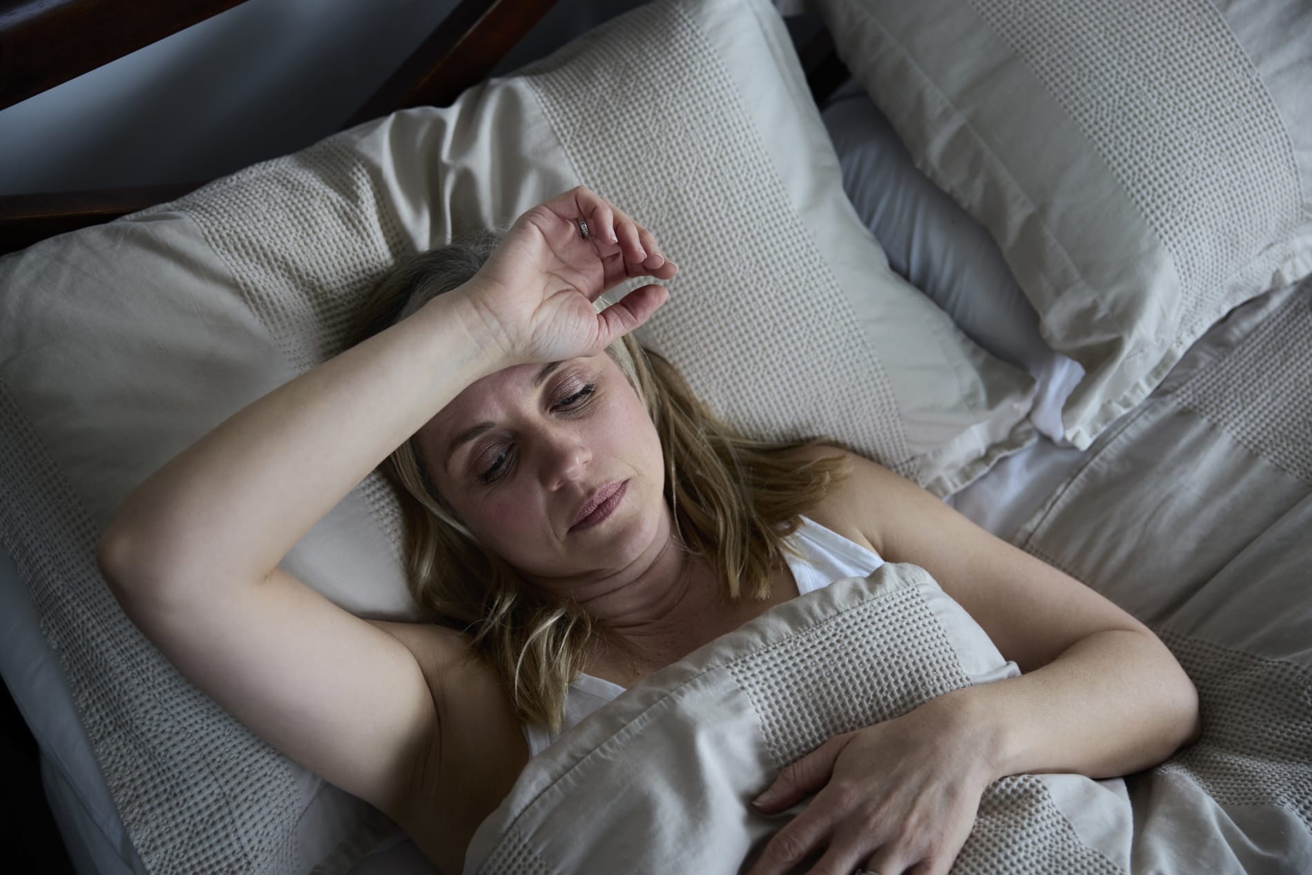 A woman laying in bed looking unwell with her hand to her head