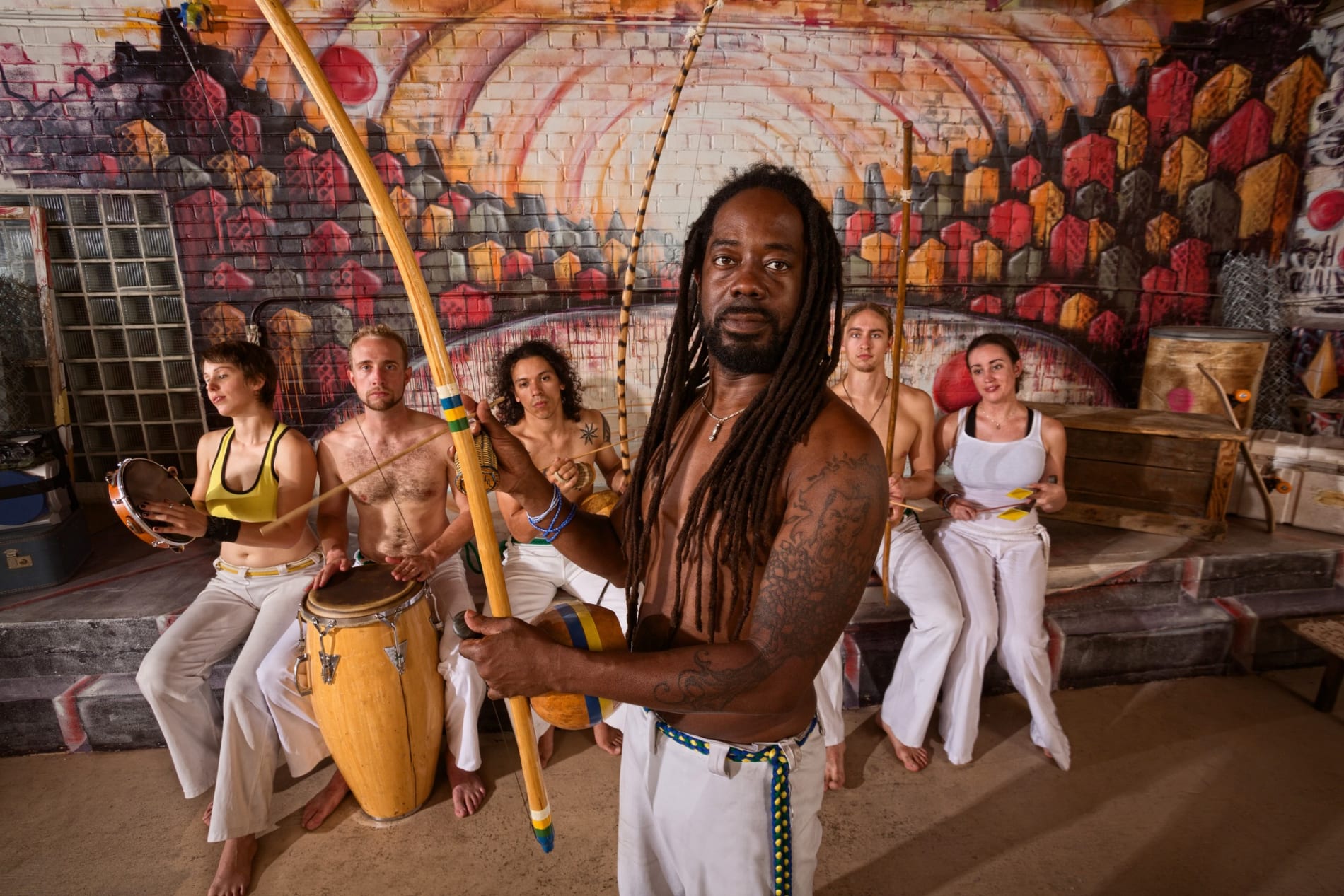 Capoeira Man with dreadlocks and instruments, with musicians behind him.
