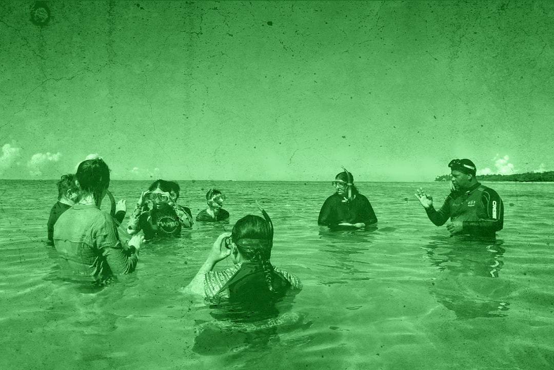 Eight GIG students listen to a local expert while snorkelling in the ocean off the coast of a Pacific Island.