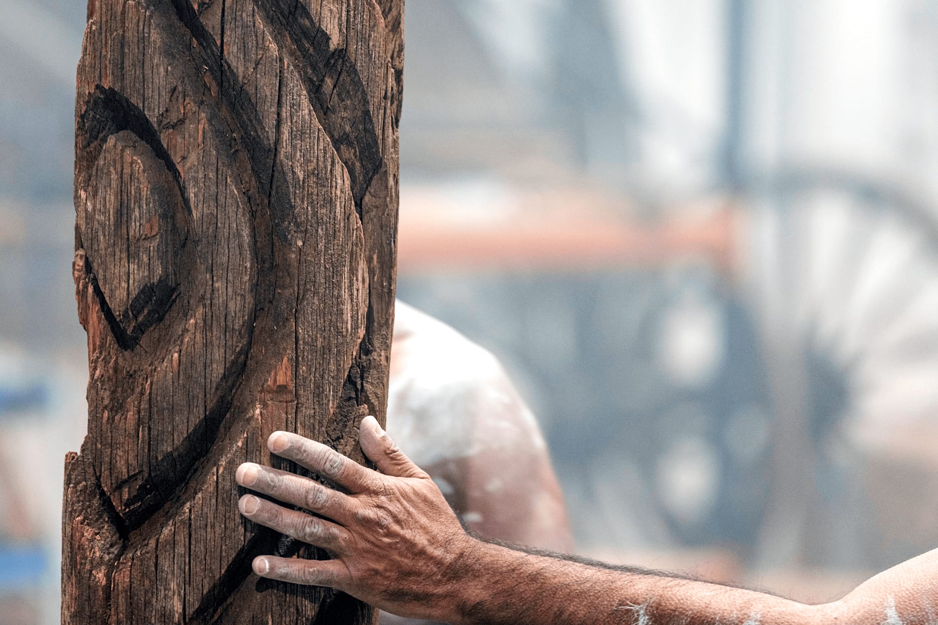 A carved sacred tree with a man's hand resting on it, smoke in the background
