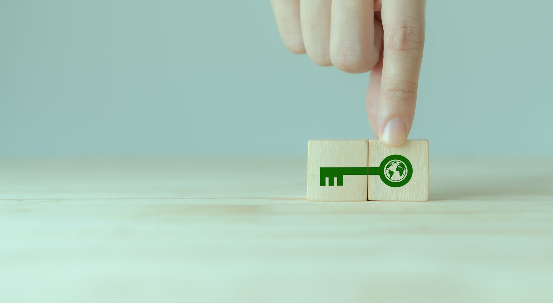 A hand putting together two small wooden blocks depicting a green key