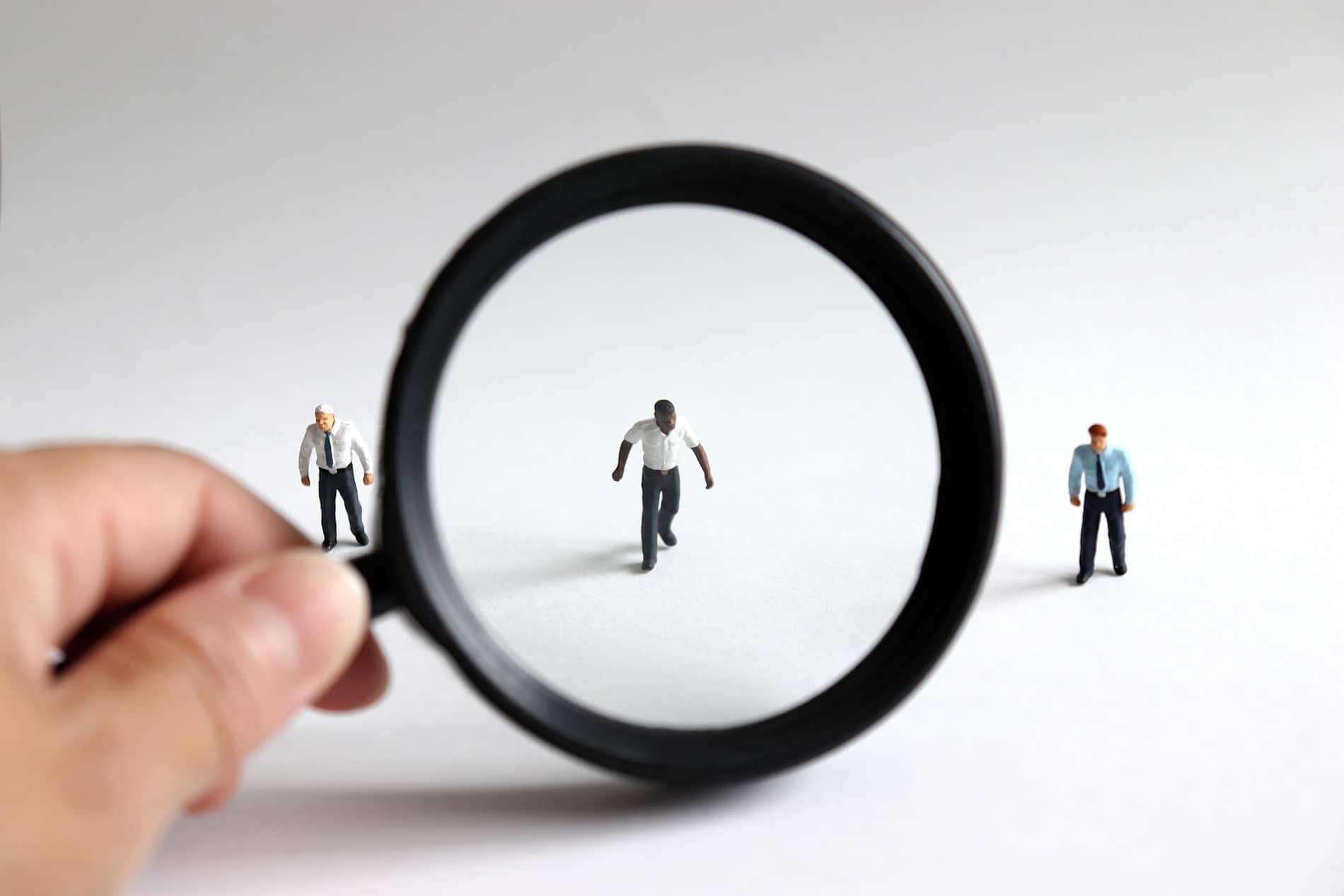 Racism concept, man looking through a magnifying glass at three figurines.