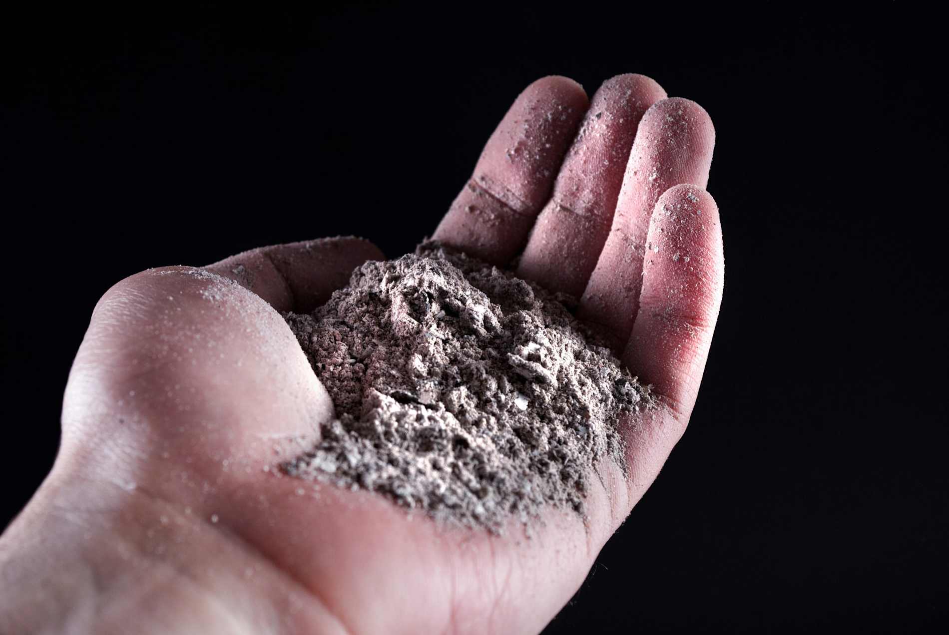 Hand holding gray ash with a black background