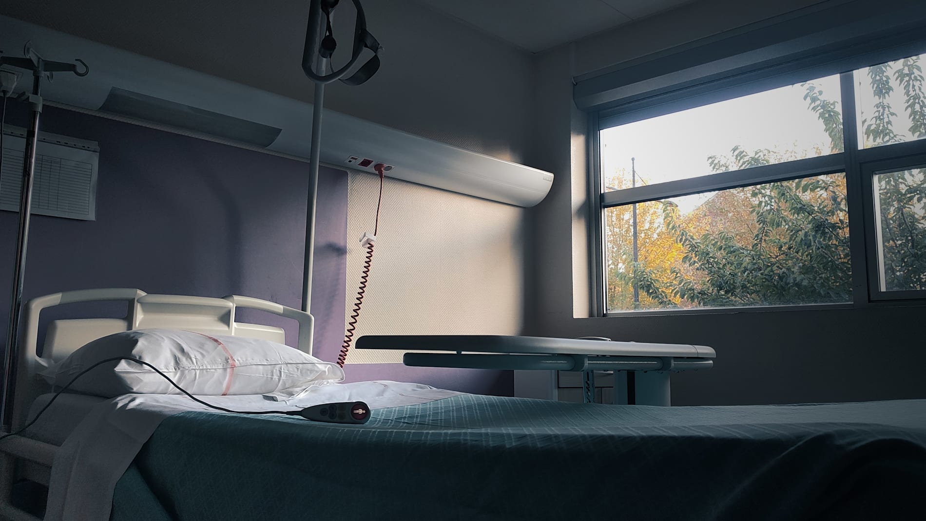 Empty hospital bed, lit by a line of light, in a sad, disquieting atmosphere