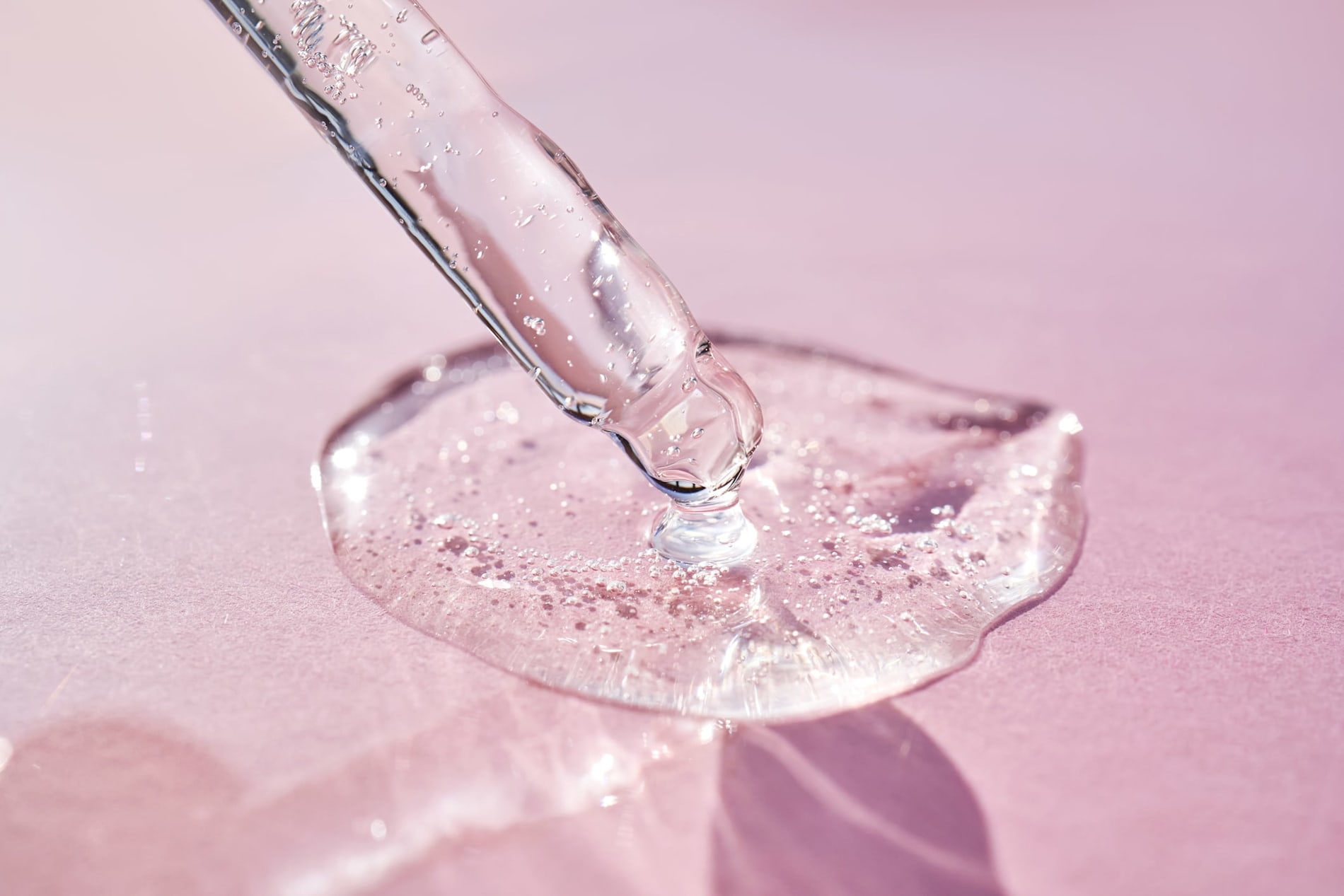 Pipette with serum shimmering in the sun on a pink background.