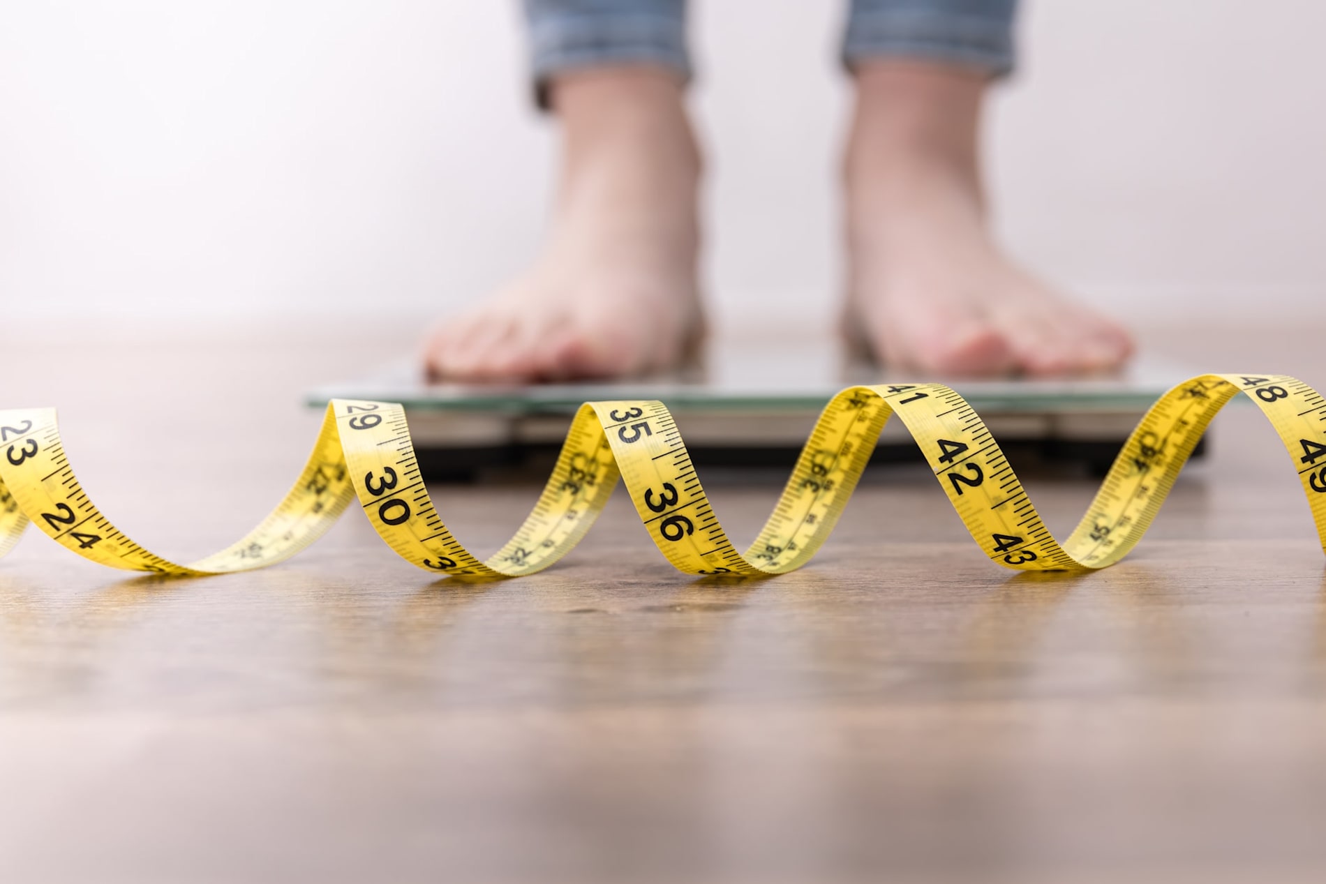 Women's legs on scales, with a close-up of a measuring tape in the foreground