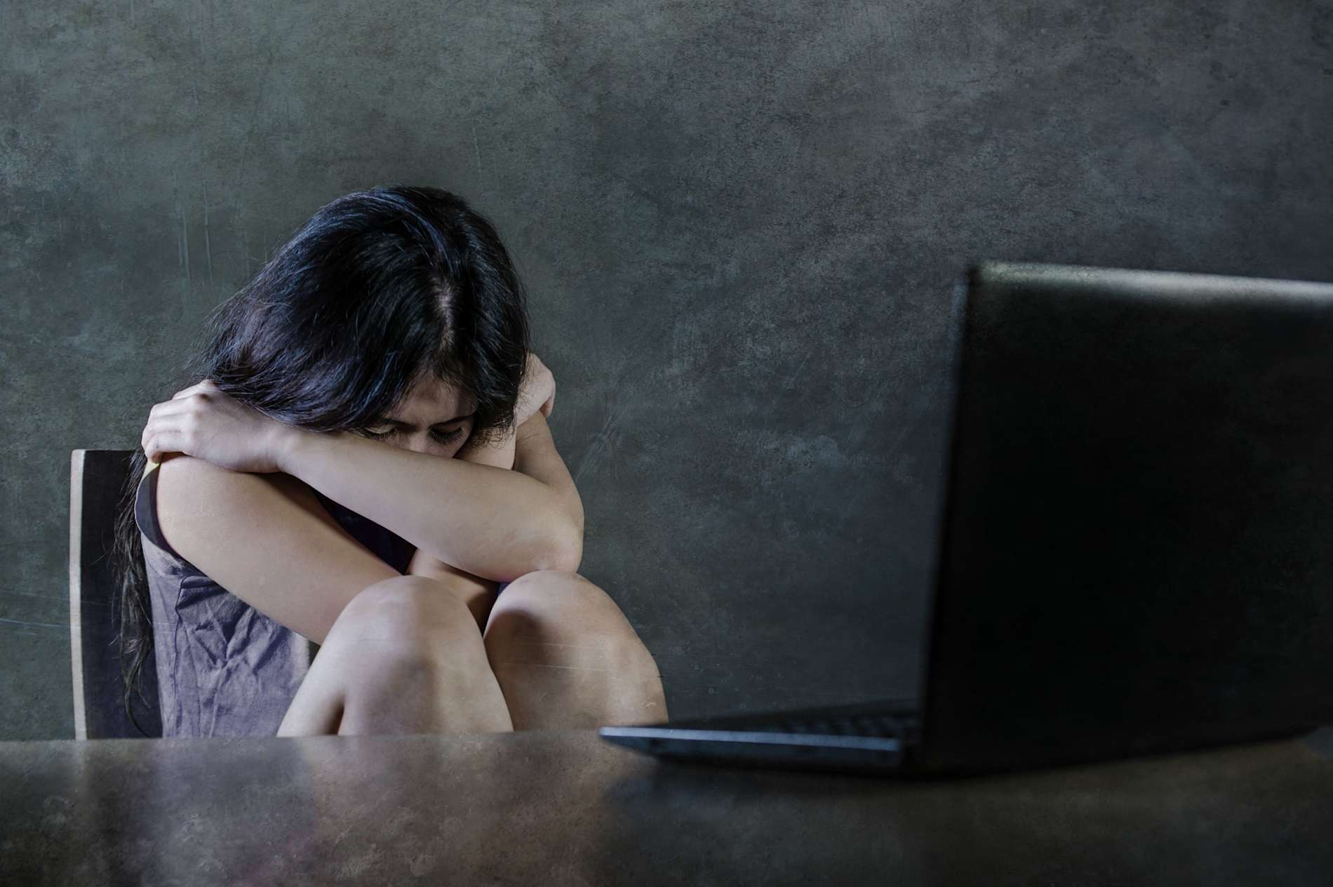 Sad and scared woman burying her head in her arms in front of an open laptop