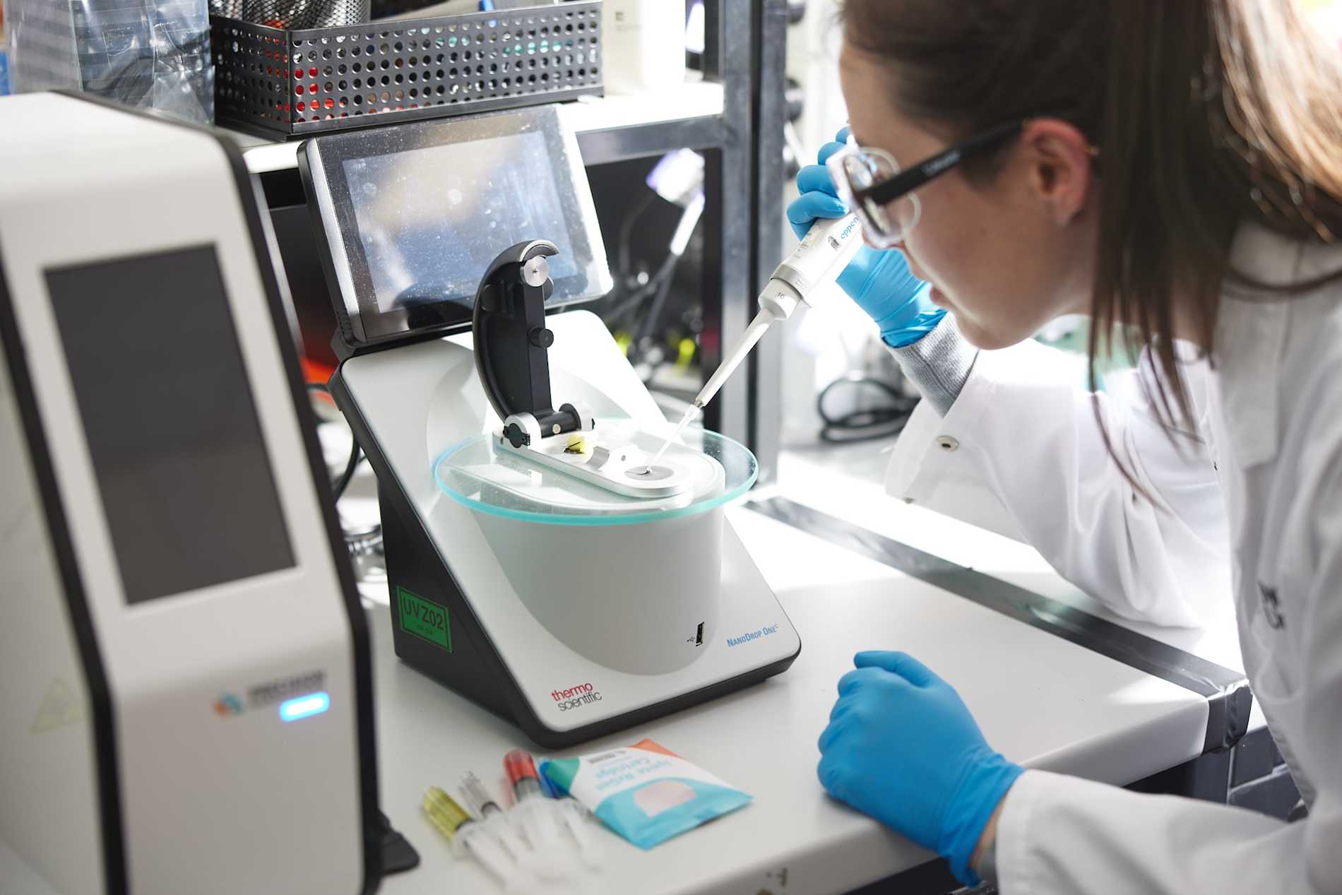 A female scientist with protective eyewear works with a pipette and analytical equipment 
