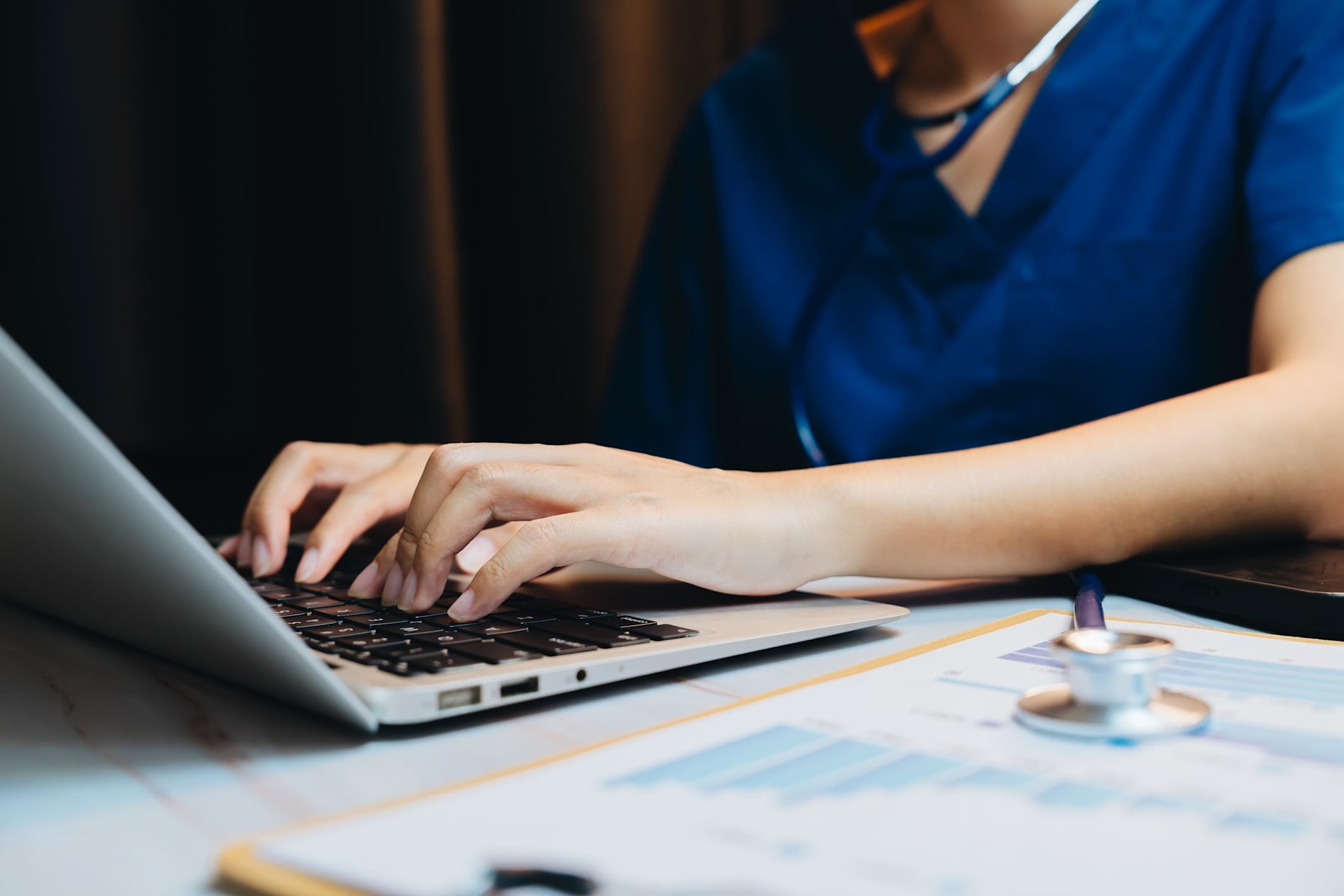 Medical professional typing on laptop in clinic with stethoscope