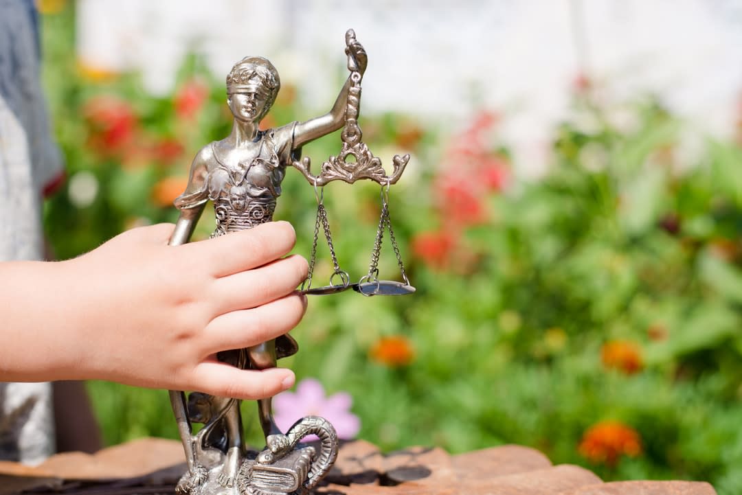 Child's hand holding sculpture of themis, femida or justice goddess on green leaves natural bokeh background