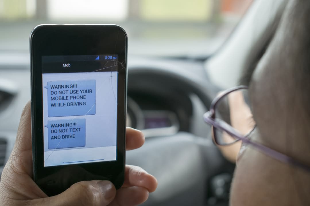 Don't Text And Drive warning on mobile phone held by a motorist.