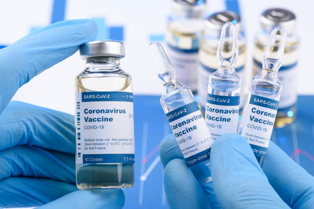 A pair of hands in covered in blue gloves holds vials of coronavirus vaccine.