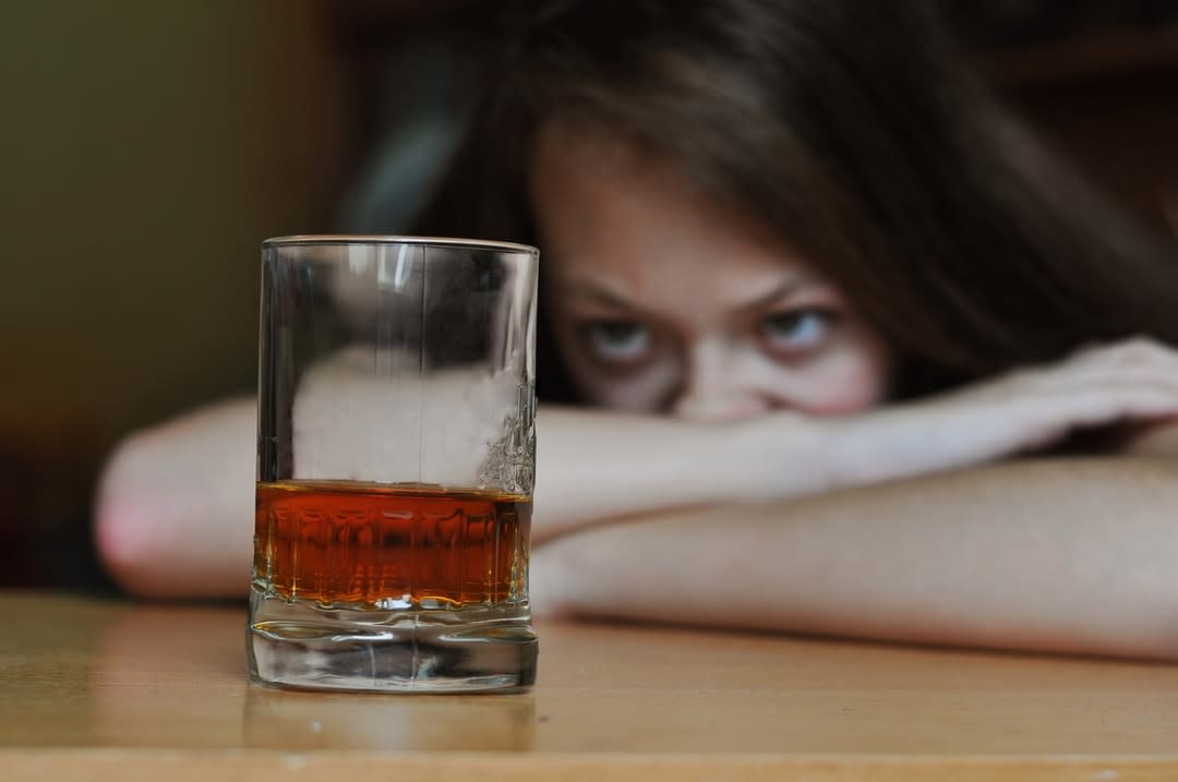 A woman at a table stares at a glass of alcohol.