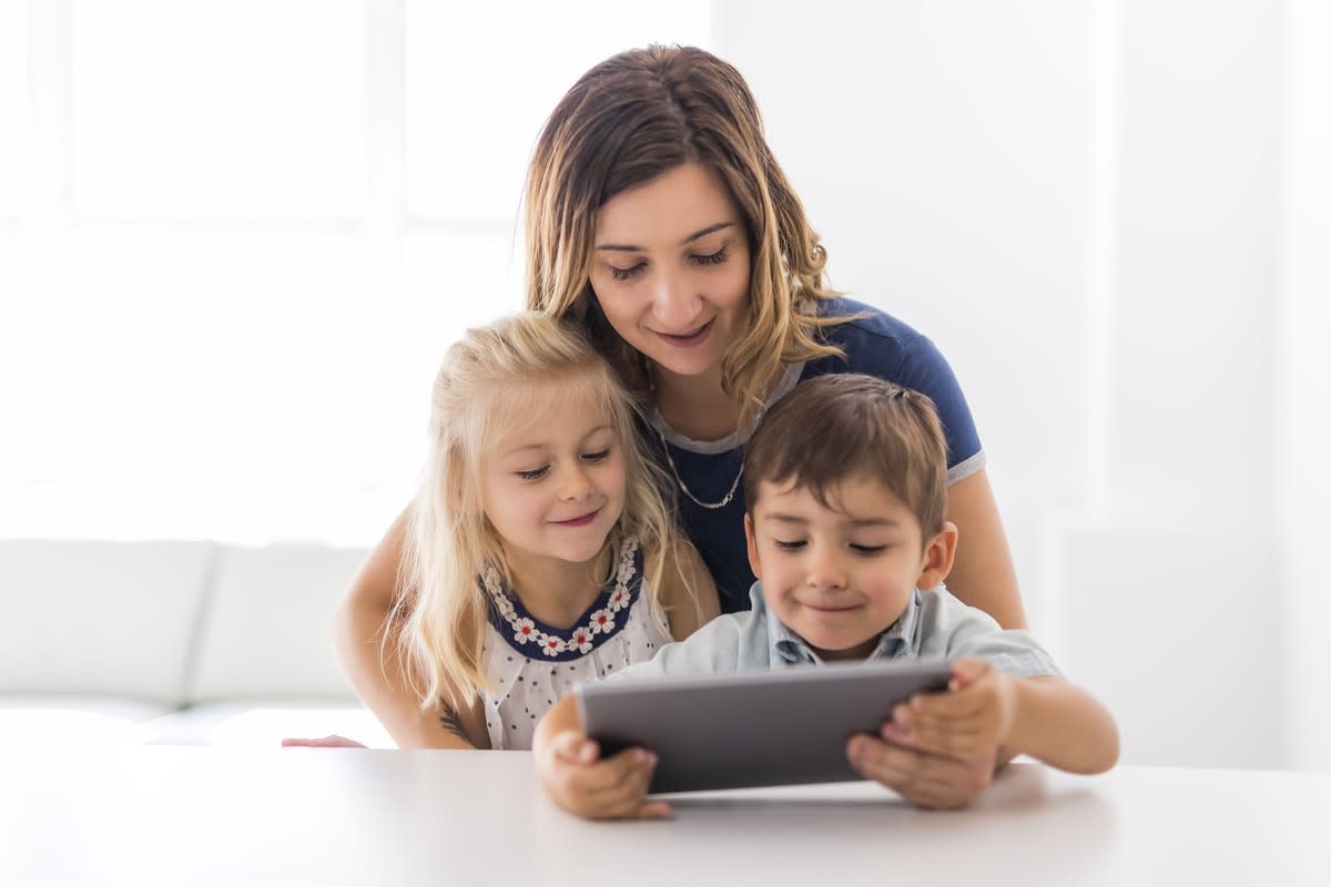 Woman hugging a young boy and girl, looking at an iPad