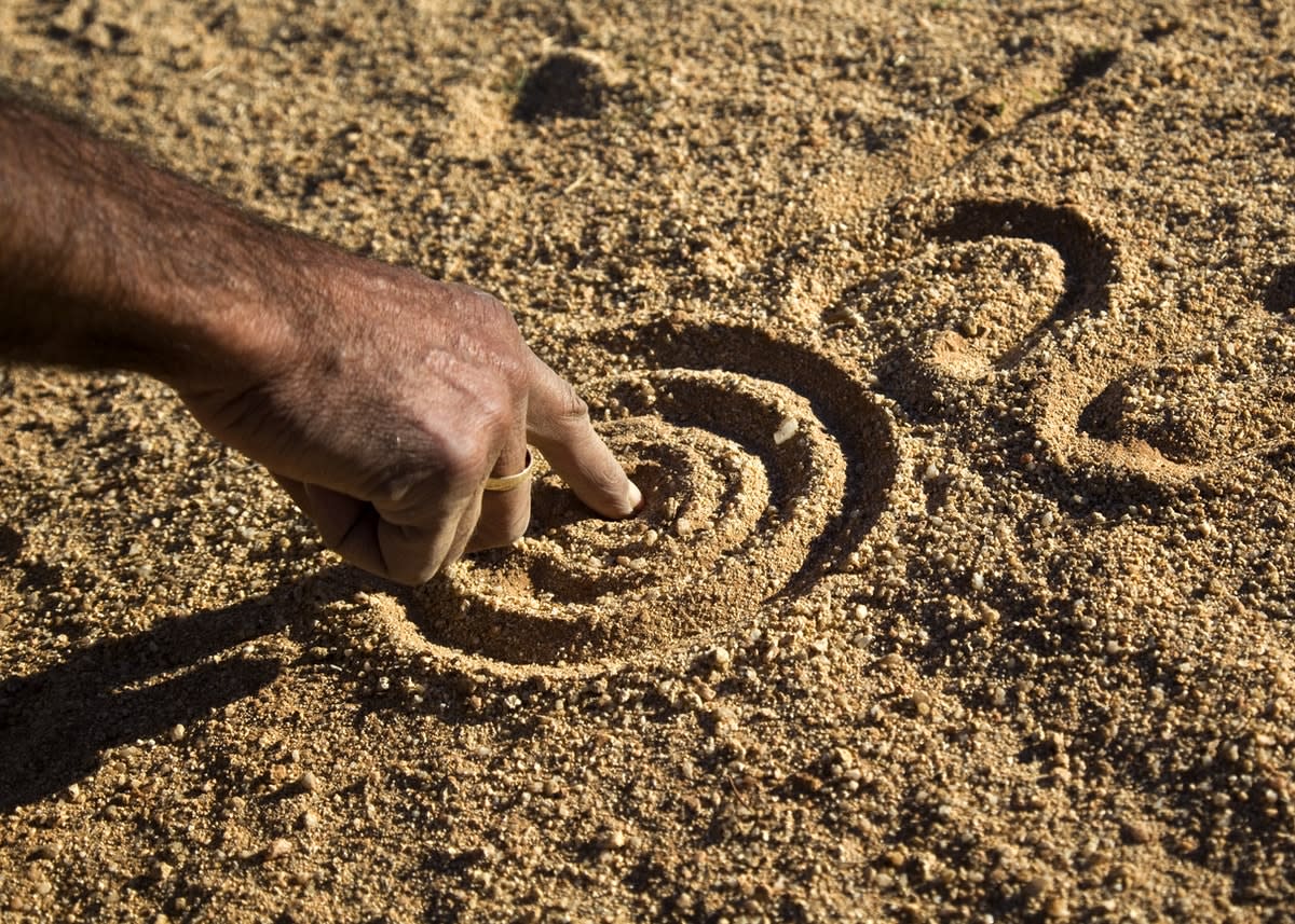 A hand drawing an Aboriginal design in the sand