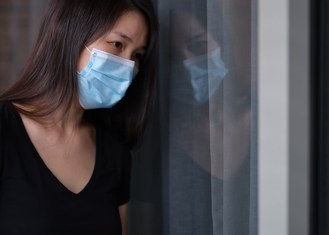 A young woman i a mask stares out the window.