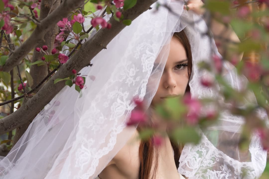 ​​​​Young bride peeking from behind crab apple tree.