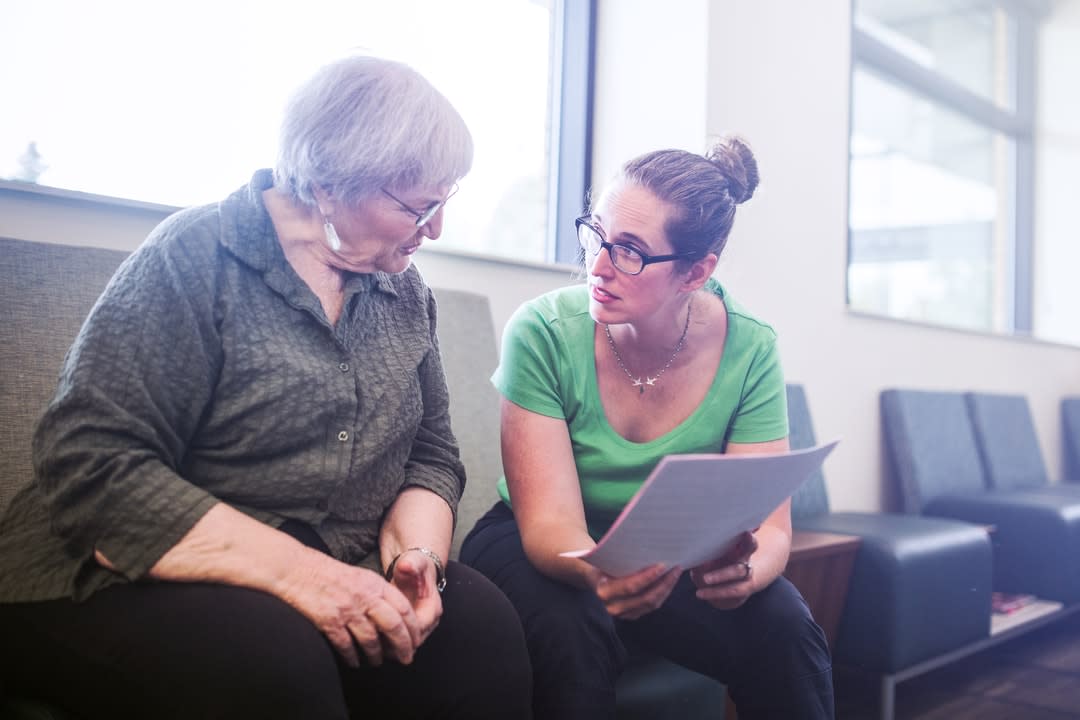 An elderly woman and doctor sitting on a seat in a hospital holding paperwork