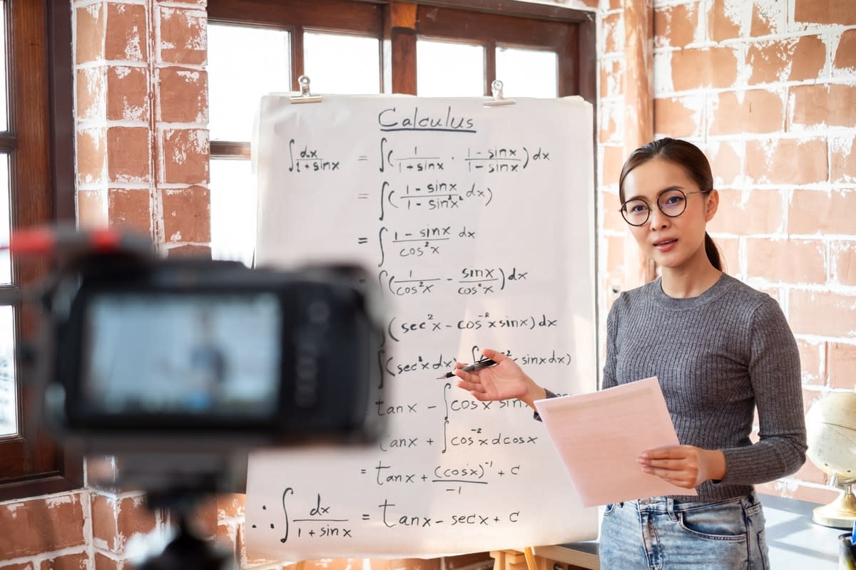 A teacher filming a maths lesson in front of a whiteboard full of equations