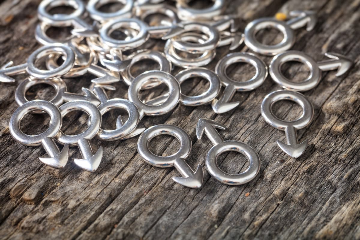 A collection of male-gender symbols made of metal, laying on wood.