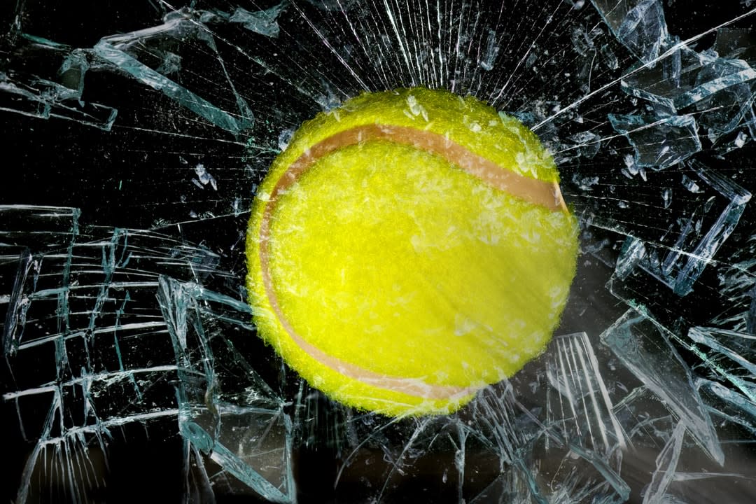 Tennis ball breaking through shattered glass