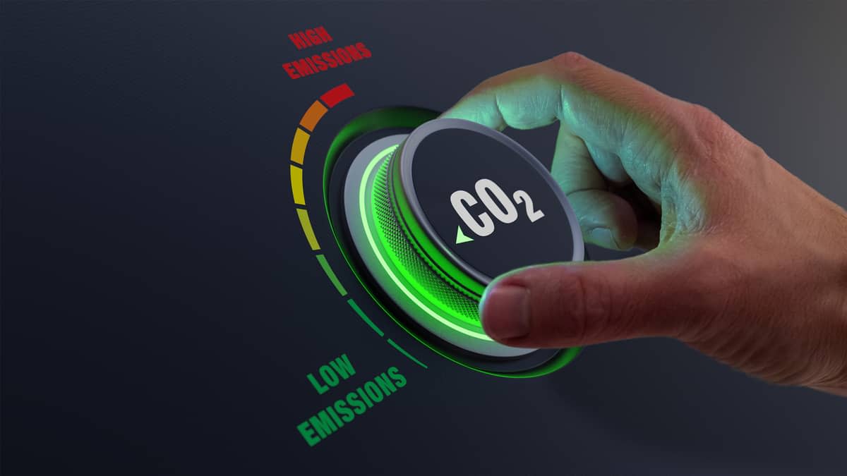 A hand turning a dial labelled ‘CO2‘, with a 'Low emissions‘ and ‘High emissions‘ range