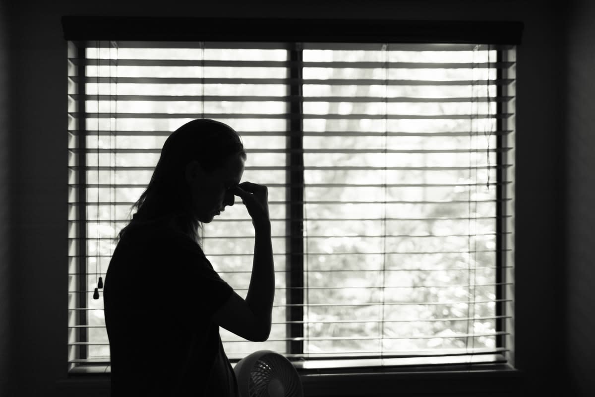 Silhouetted woman in front of a window looking distressed, holding her hand to her head 