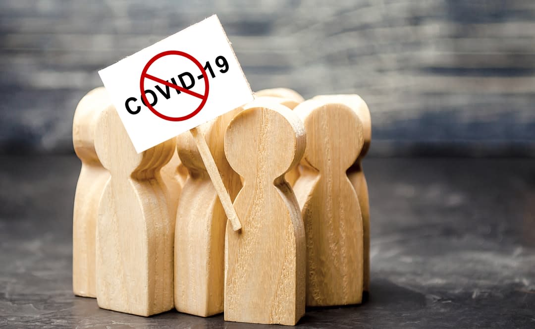 Wooden figures huddled around a COVI-19 denial sign.