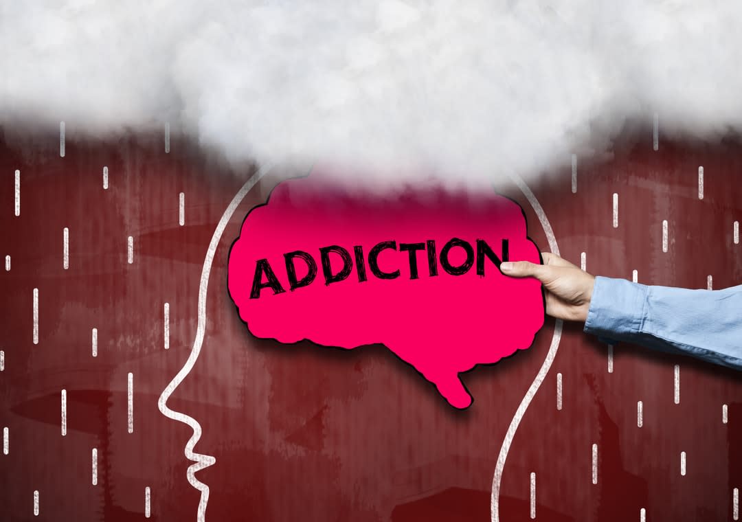 The outline of a person's head with a brain-shaped sign with the word addiction written on it