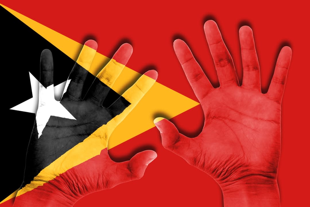 A pair of hands set against the background of a Timor-Leste flag.