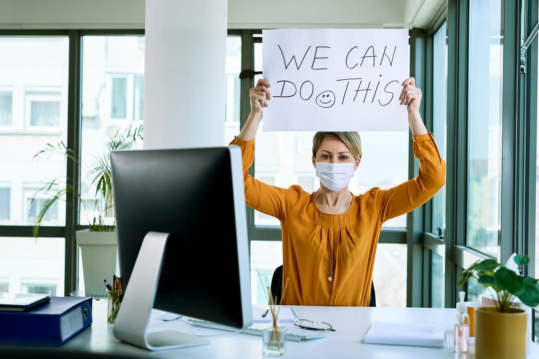 A woman sitting at an office holds up a sign saying: We can do this.