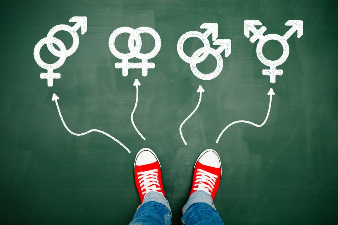 Gender fluidity concept showing a child's feet in red sneakers and gender symbols on a blackboard background.