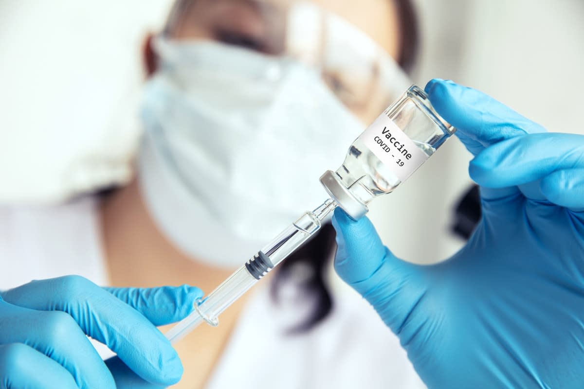 Female scientist in protective mask, glasses and gloves draws Covid-19 vaccine into the syringe.