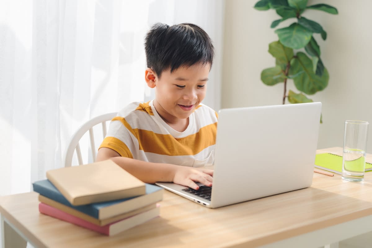 A young Asian boy doing schoolwork on a laptop at home