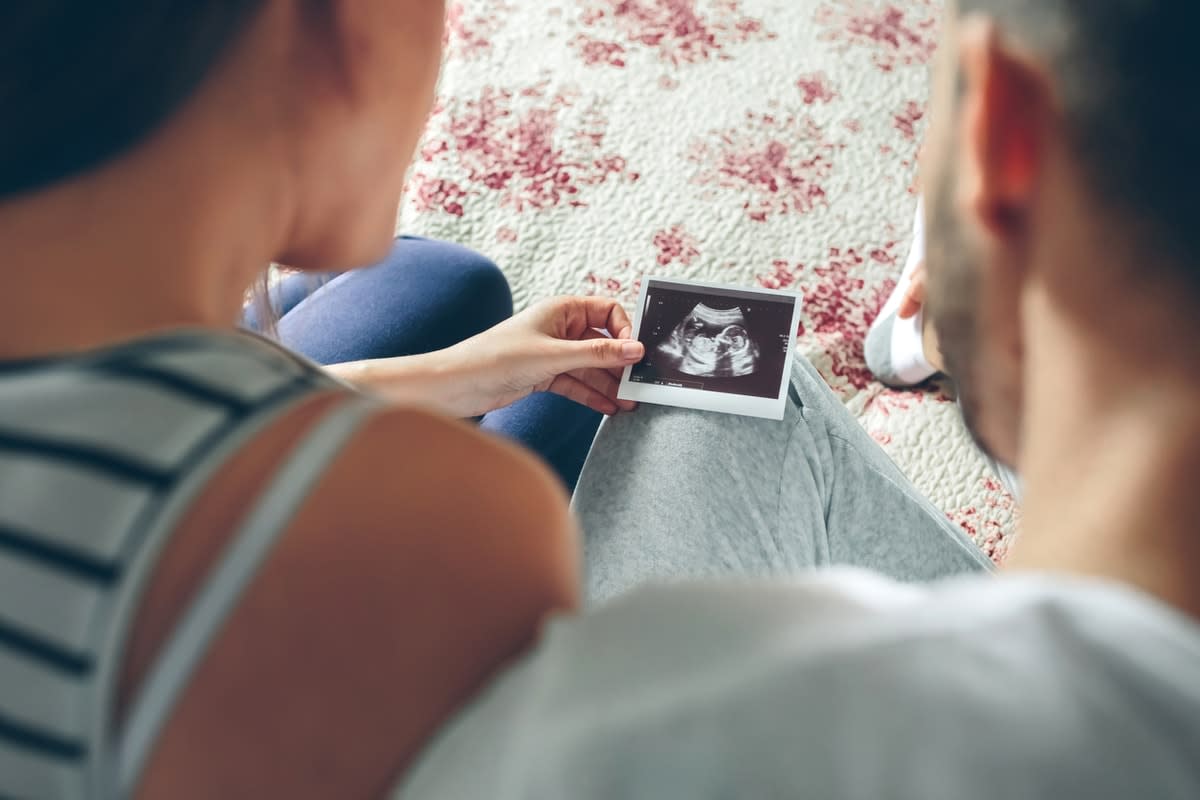 Overhead photo from behind of a couple looking at an ultrasound image of a baby