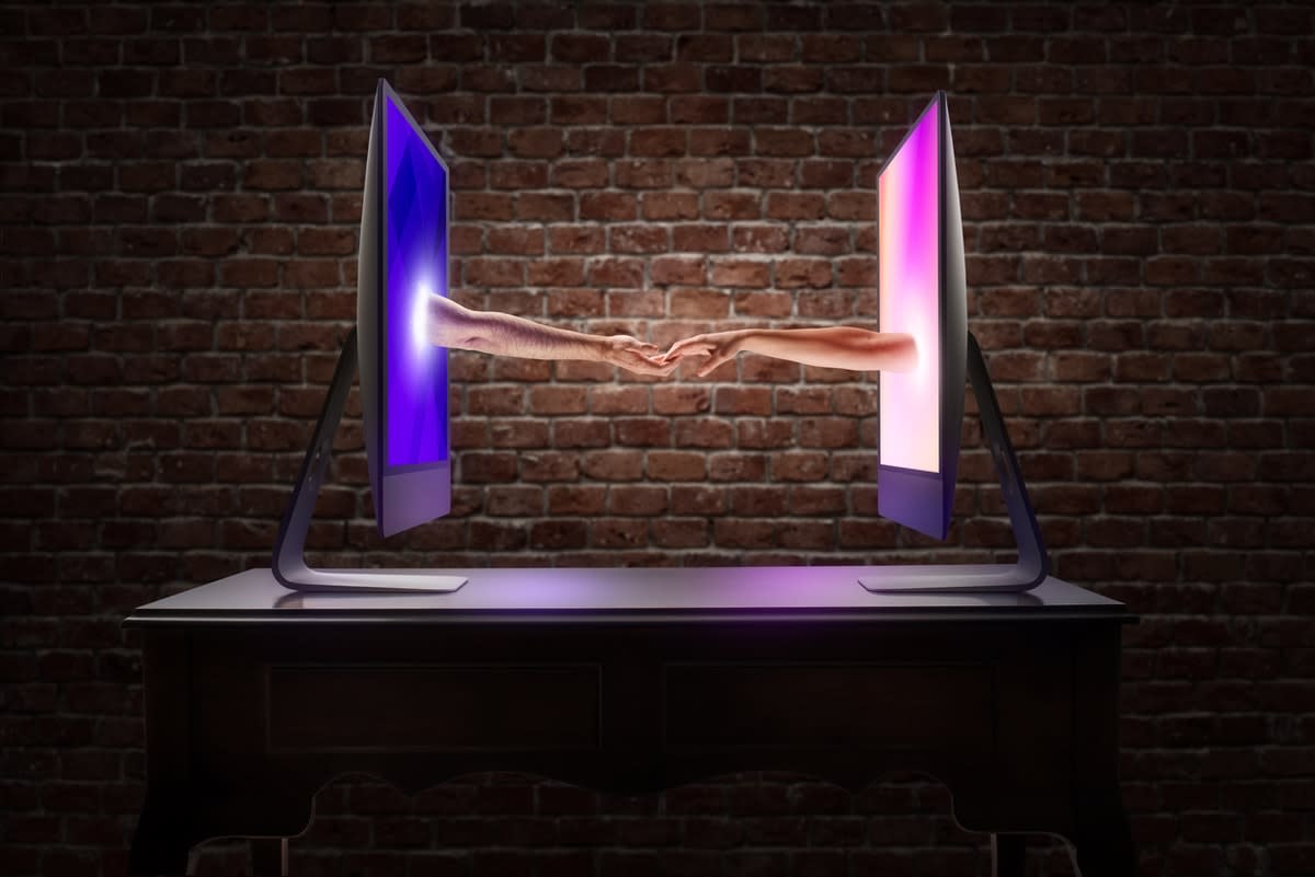 Two computer monitors facing each other, with arms reaching out of each to hold hands