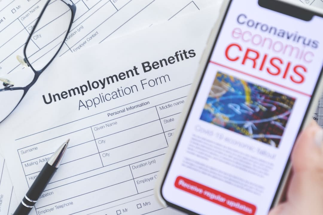 Close up of a mobile phone with Coronavirus covid-19 economic crisis news article. There is an unemployment benefits claim form in the background