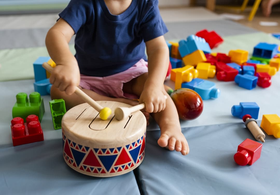 A young child in childcare bangs ion a drum.