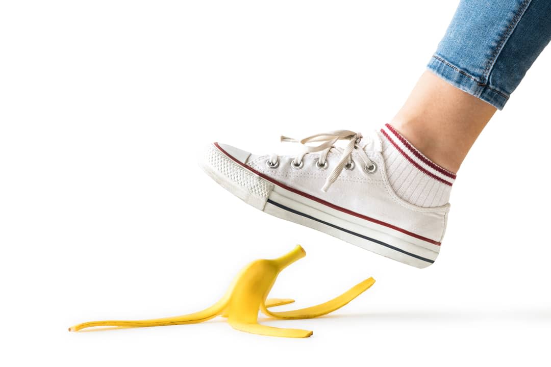 A woman in white sneakers about to step on a banana peel.