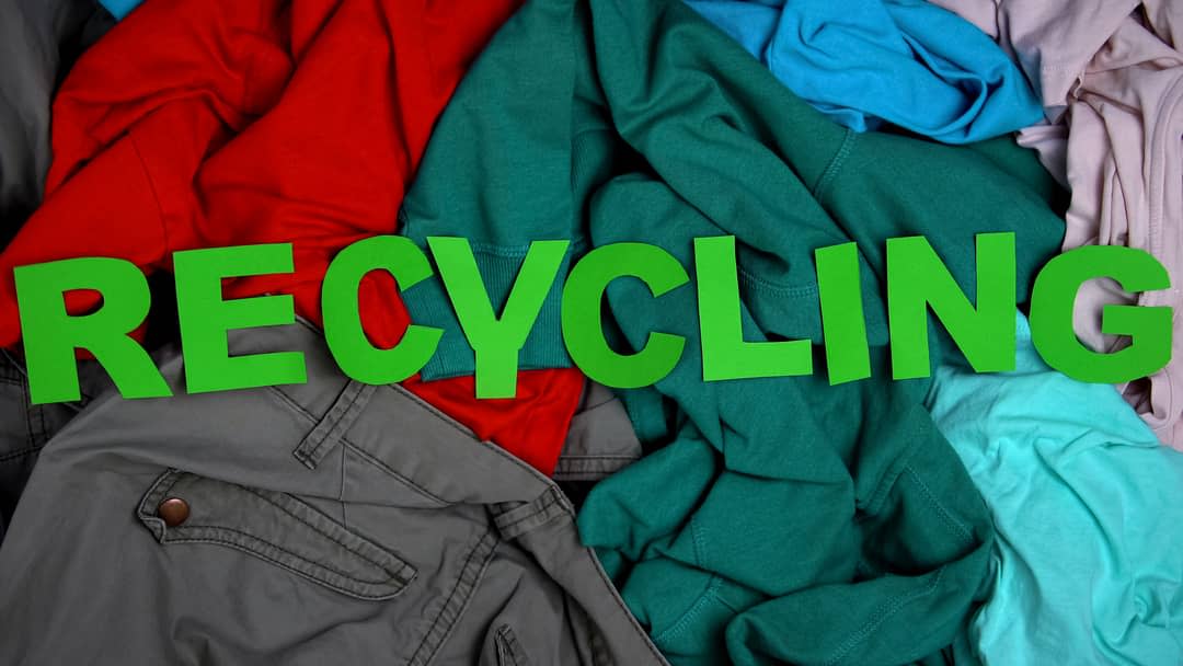 A pile of clothes topped with the word RECYCLING in cutout letters