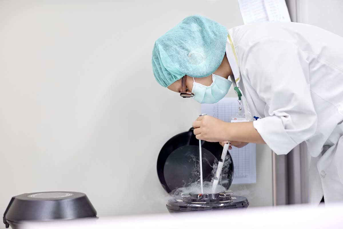 A masked medical worker leaning over a sperm and egg-freezing vat 