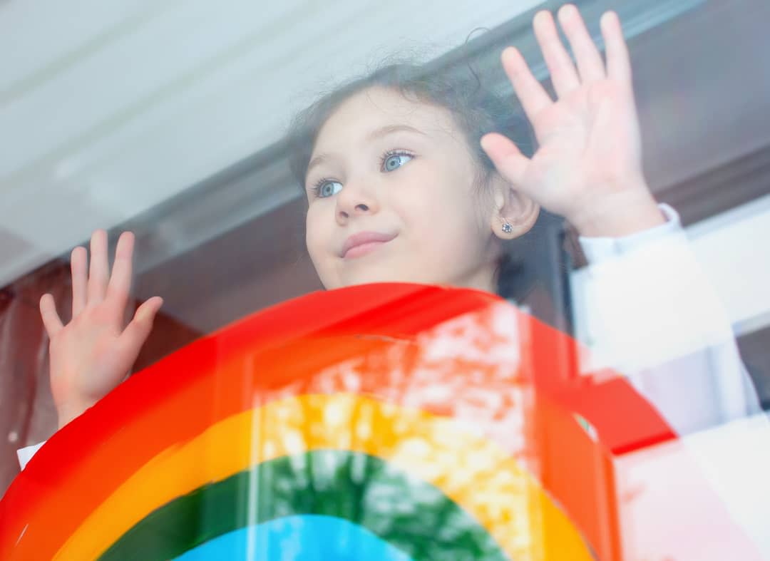 Little girl with hope looks out the window on which a rainbow is painted