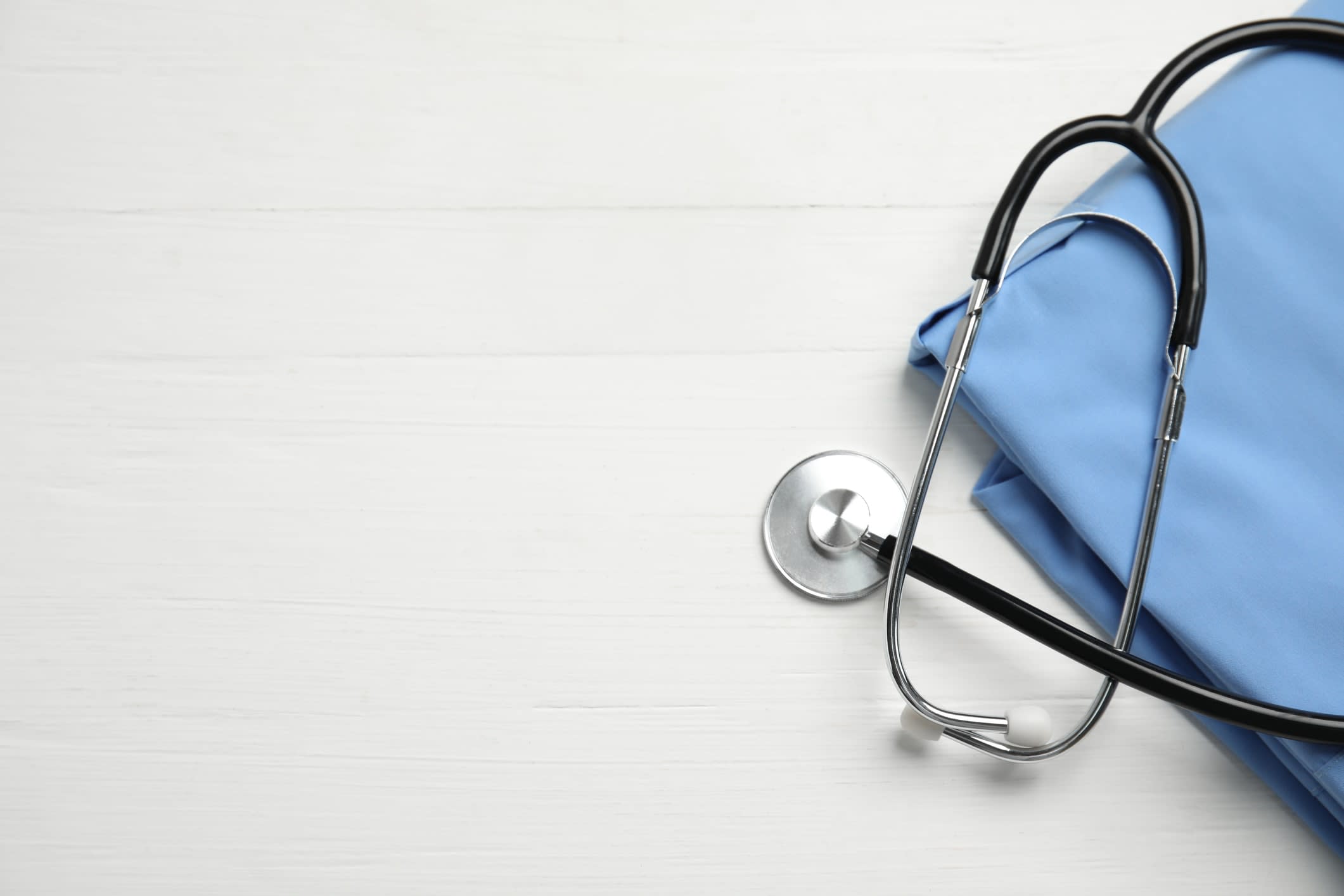 A stethoscope and folded blue uniform sitting on white background