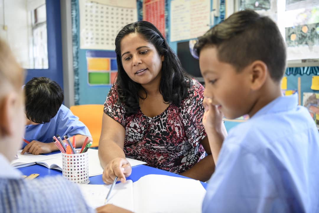 A teacher in a classroom helping a young student.